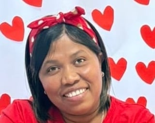 Smiling woman with long dark hair wearing a red bow headband and red shirt against a light blue background with red heart decorations