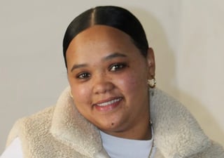 Portrait of a smiling woman with dark hair pulled back, wearing a cream-colored shearling collar over a white shirt and pearl earrings