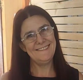 Woman with long dark hair and glasses smiling at camera indoors