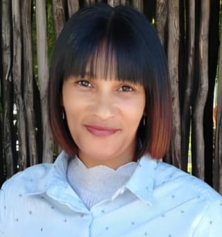 Woman with black and rust ombre hair with bangs wearing light blue button-up shirt against wooden fence background