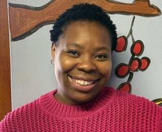 Smiling woman wearing a pink sweater poses for portrait photo against wall with decorative artwork.